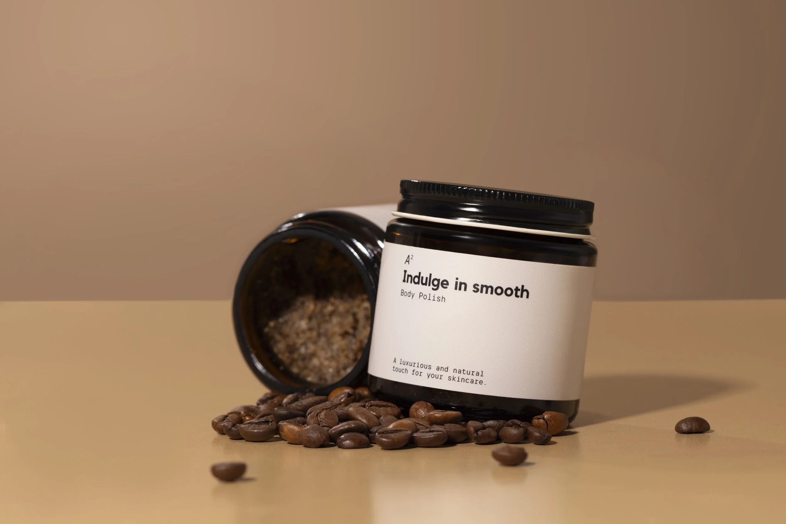 A container of body polish with a black lid and a white label, surrounded by scattered coffee beans with some spilled around it.