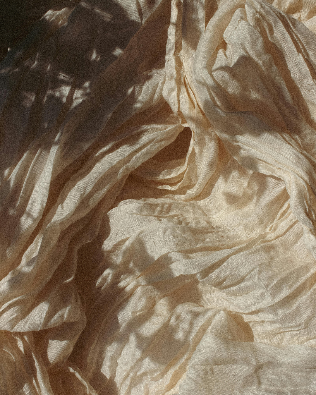 Close-up of crumpled light-colored fabric with shadows and folds.