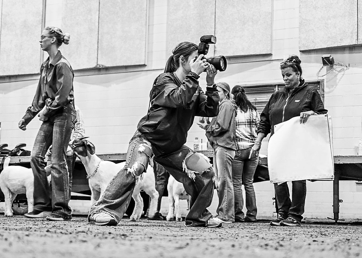 A livestock photographer taking backdrop photos of a show goat at a livestock show. Several other women, some standing and one holding a Champion banner at a livestock jackpot show in Vernal Utah.