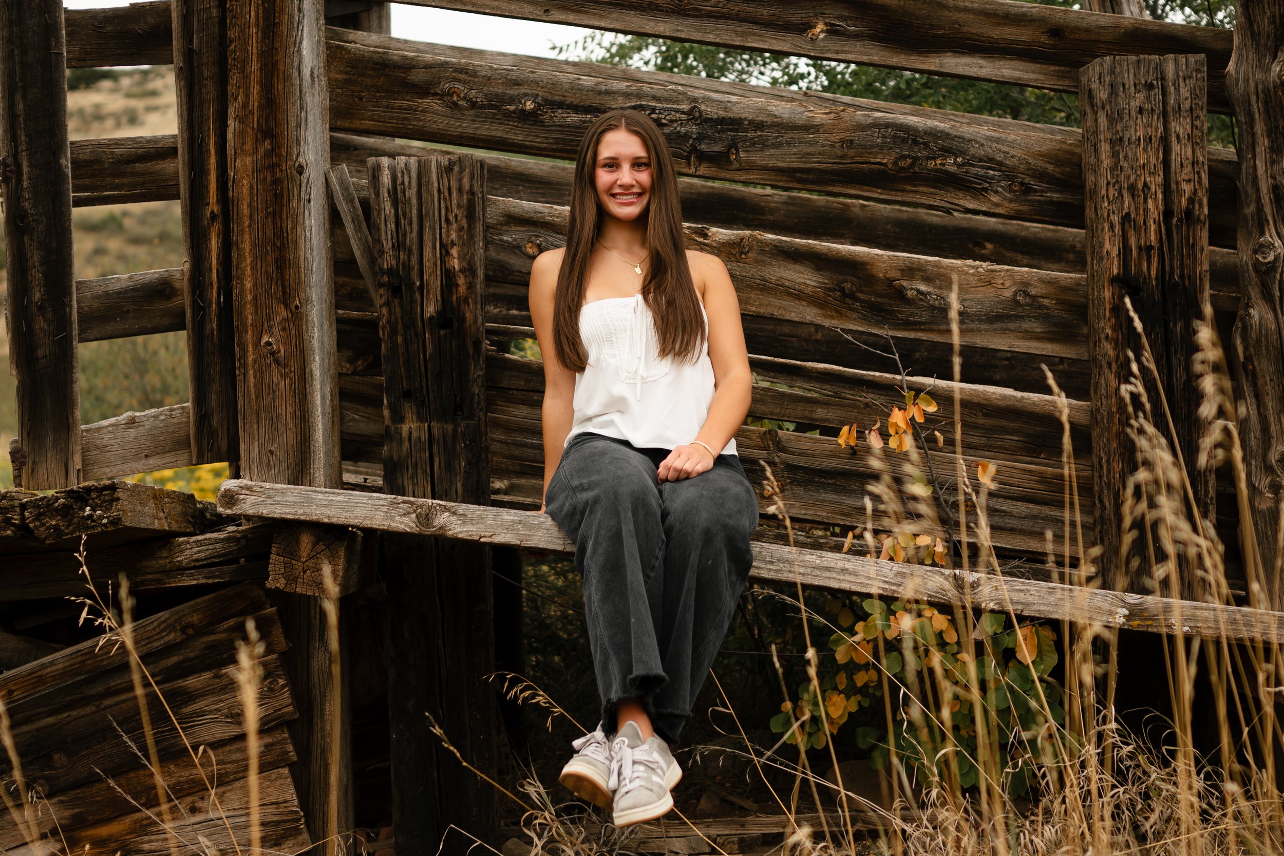A high school senior girl sitting on a cattle chute in Fort Collins, Colorado. She is wearing a white strapless top and black jeans. 