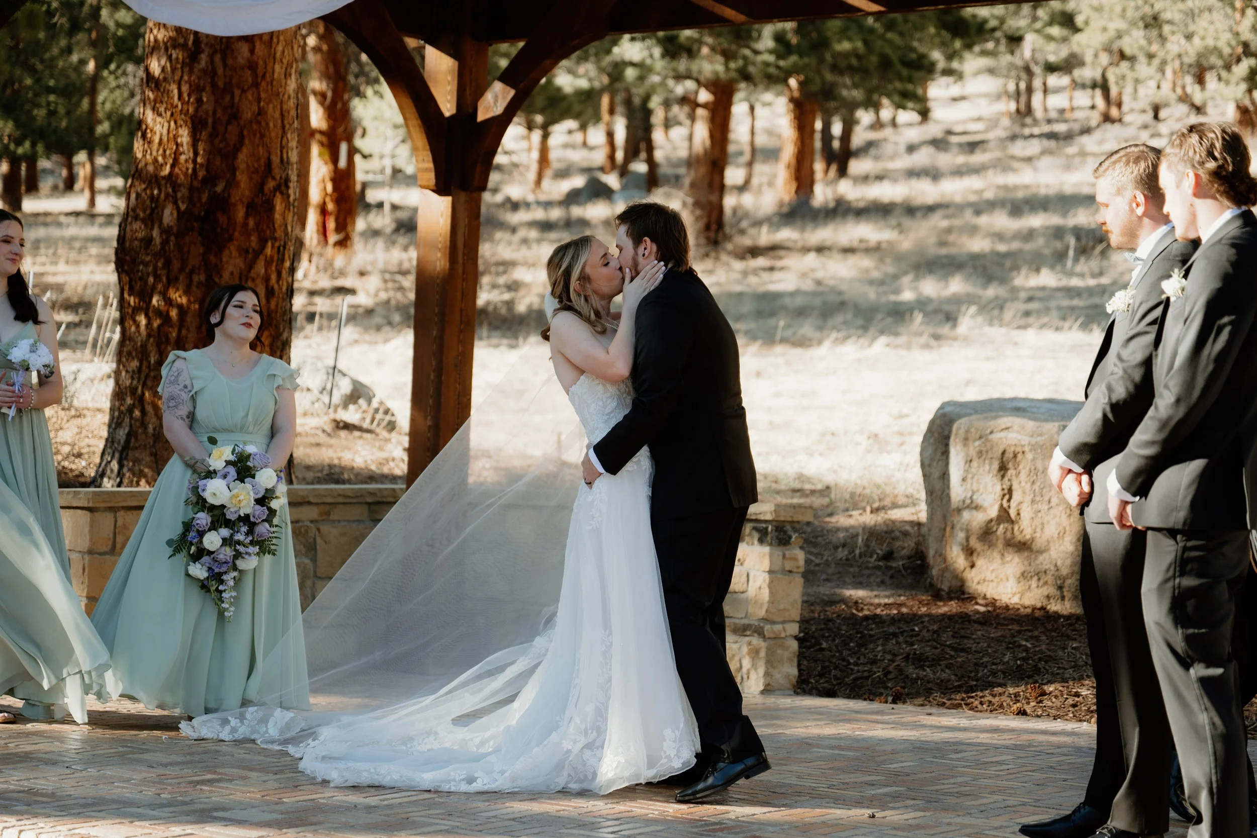 Outdoor march wedding ceremony in Estes Park at Della Terra by Wedgewood. Bridesmaids dresses sage green, florals lilac.