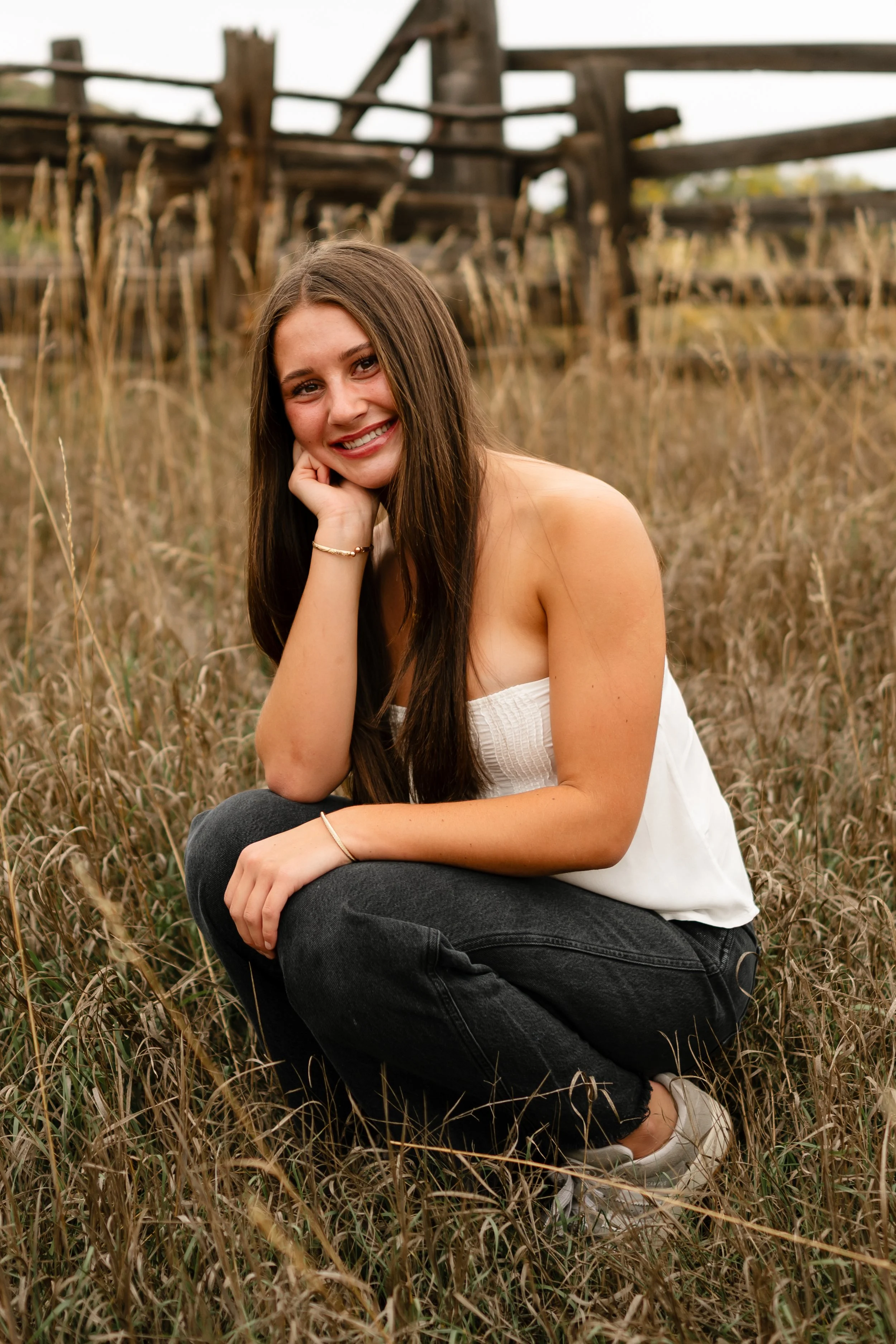 A high school senior girl sitting in a field in Fort Collins, Colorado at Horsetooth. She is wearing a white strapless top and black jeans. 