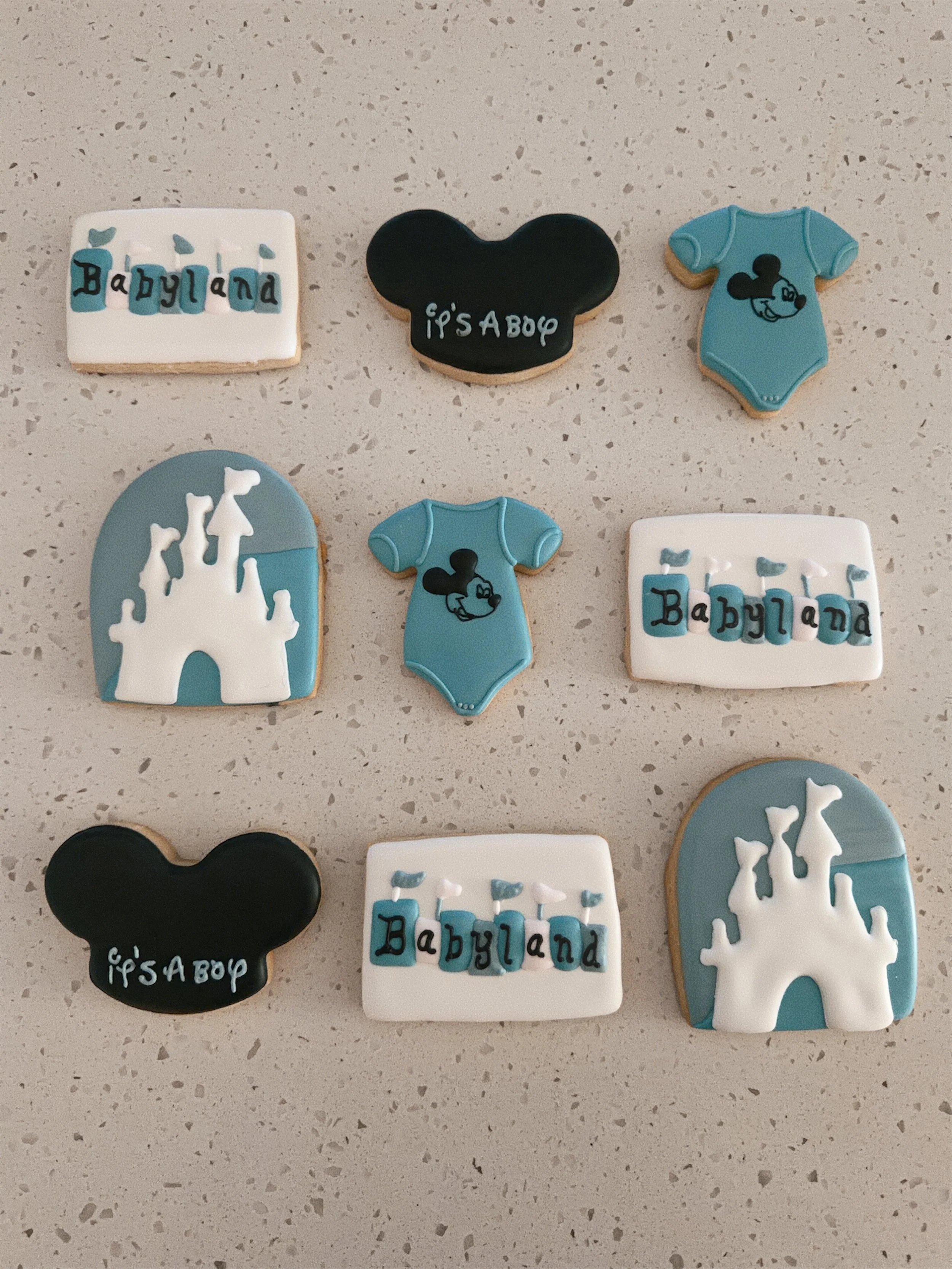 Variety of decorated cookies with Disney and baby-themed designs, including Mickey Mouse silhouettes, castles, and the words "Babyland" and "It's A Boy" on the cookies.