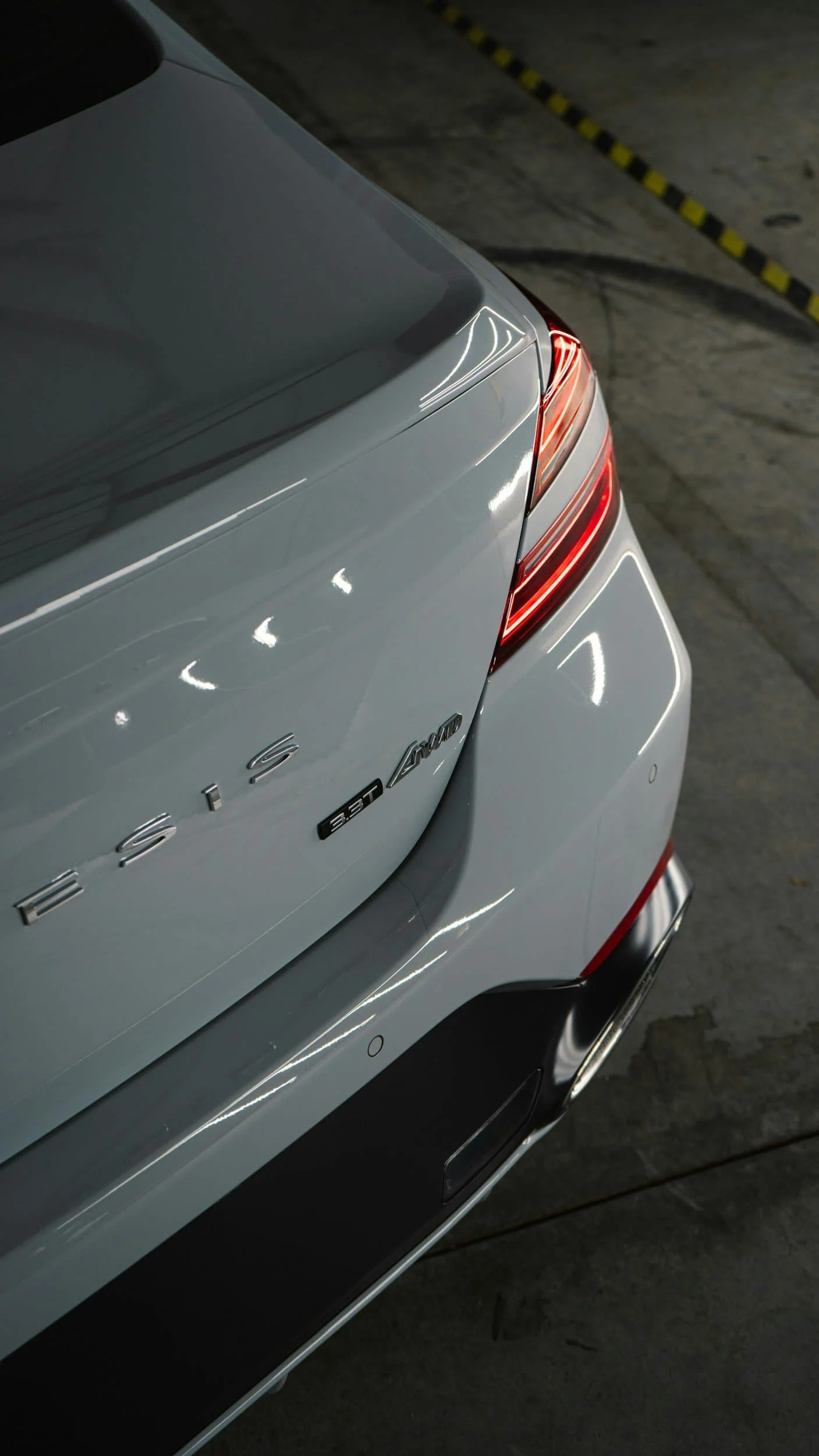 Close-up of the rear of a white Genesis G80 3.5T car, showcasing its taillight and model badges in a dimly lit garage.