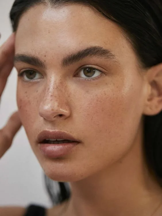 Close-up of a woman with natural makeup, freckles, and dark hair, looking to the side.