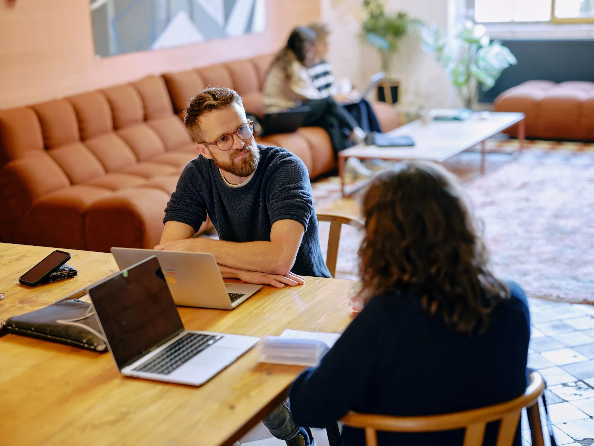 Mitarbeitende sitzen mit Laptops an einem Tisch und sprechen miteinander in einem Gemeinschaftsraum
