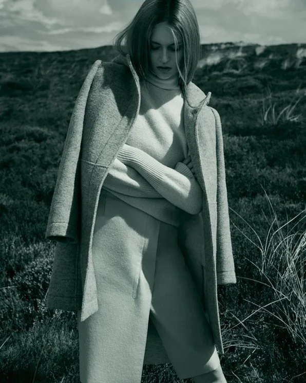 Schwarzweiß-Momentaufnahme für Hessnatur x ELLE: Model in cozy Wolloutfit mit verschränkten Armen auf einer Bergwiese, umgesetzt von imagespy.