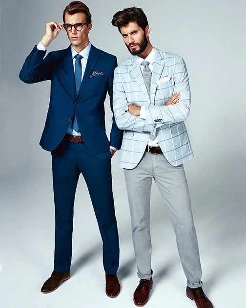GQ Promotion by imagespy: Zwei Male Models, einer im mittelblauen Anzug mit Brille, der andere in kariertem Sakko und grauer Jeanshose mit verschränkten Armen, Studioaufnahme für SIR OLIVER.