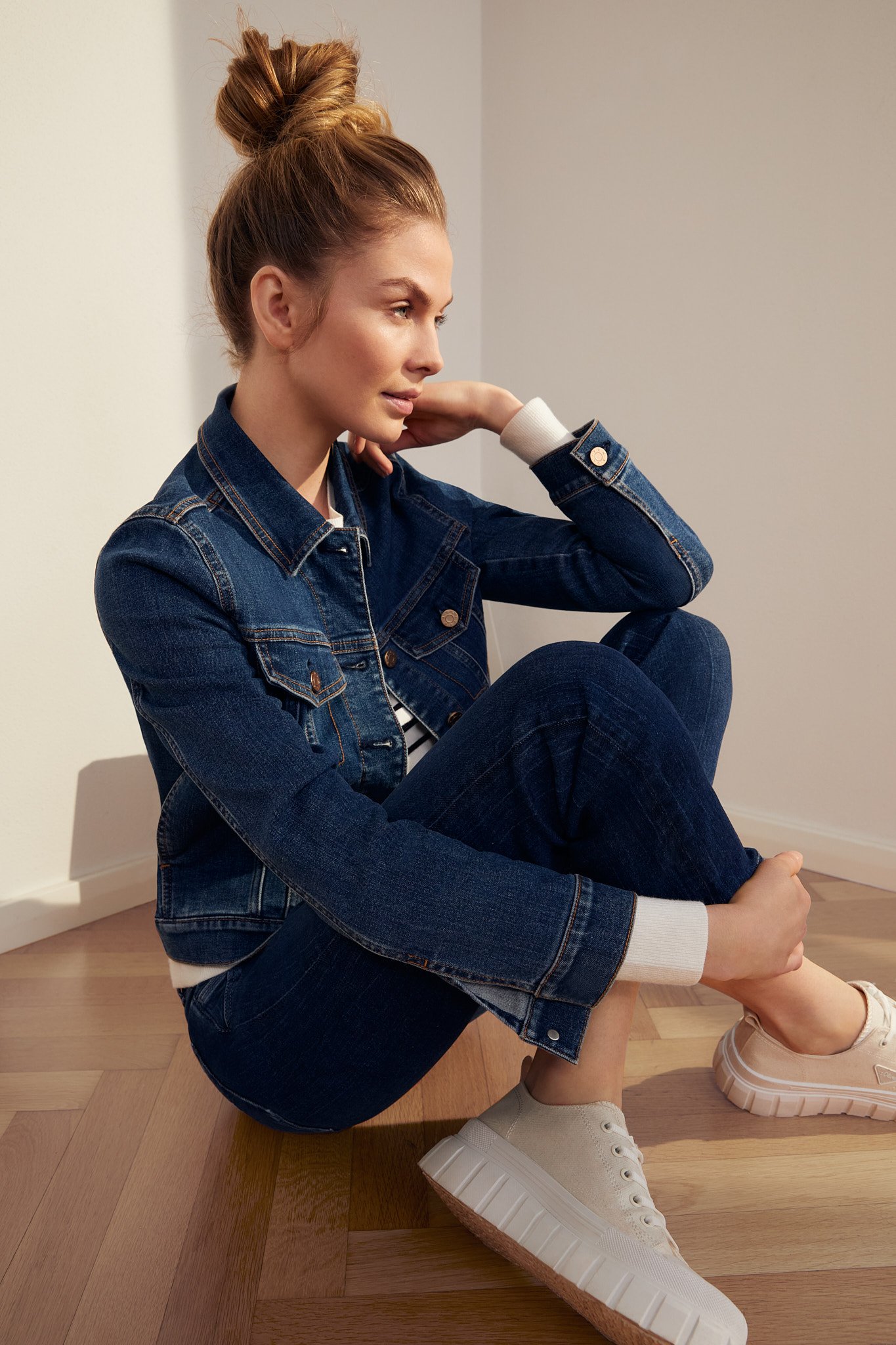 Content-Fotoshooting für s.Oliver Denim: Model sitzt auf dem Boden in dunkelblauer Jeanshose, passender Jeansjacke und weißen Sneakern; umgesetzt von imagespy.