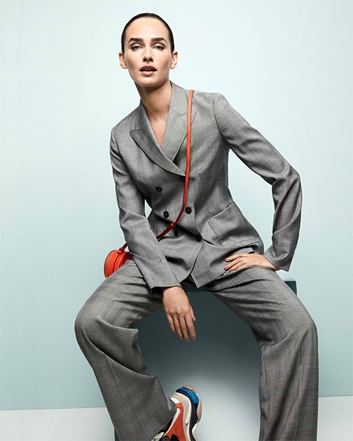 Studioaufnahme 2019 für Lodenfrey in ELLE: Model sitzend in grauem Windsor-Anzug mit orangefarbener Tasche – luxuriöse High-End-Fashion-Inszenierung von imagespy.