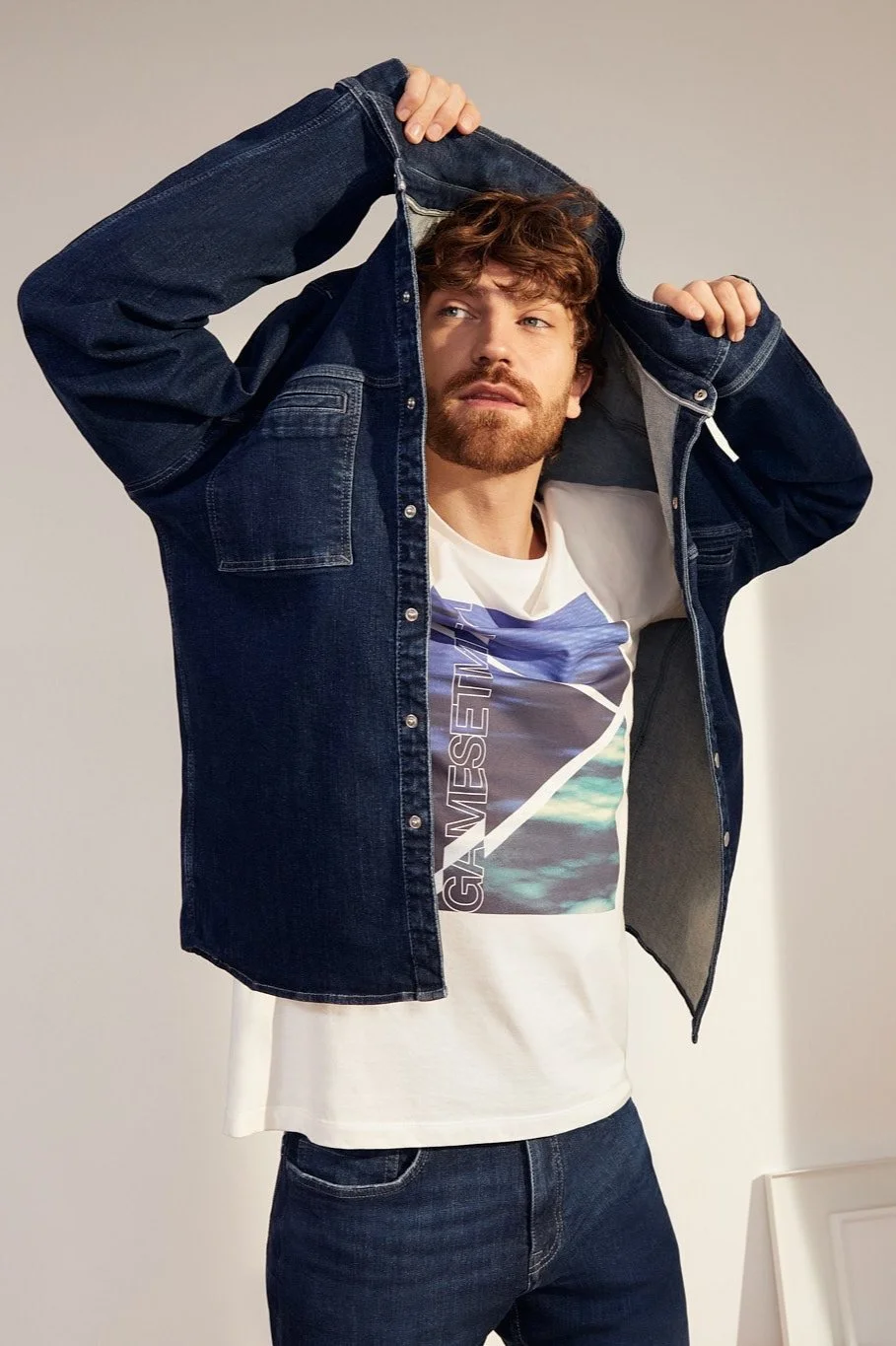 Content-Fotoshooting für s.Oliver Denim: Stehendes Male Model zieht Dark-Denim-Hemd über den Kopf, darunter T-Shirt; casual, modern, lässiger Social-Media-Look, umgesetzt von imagespy.