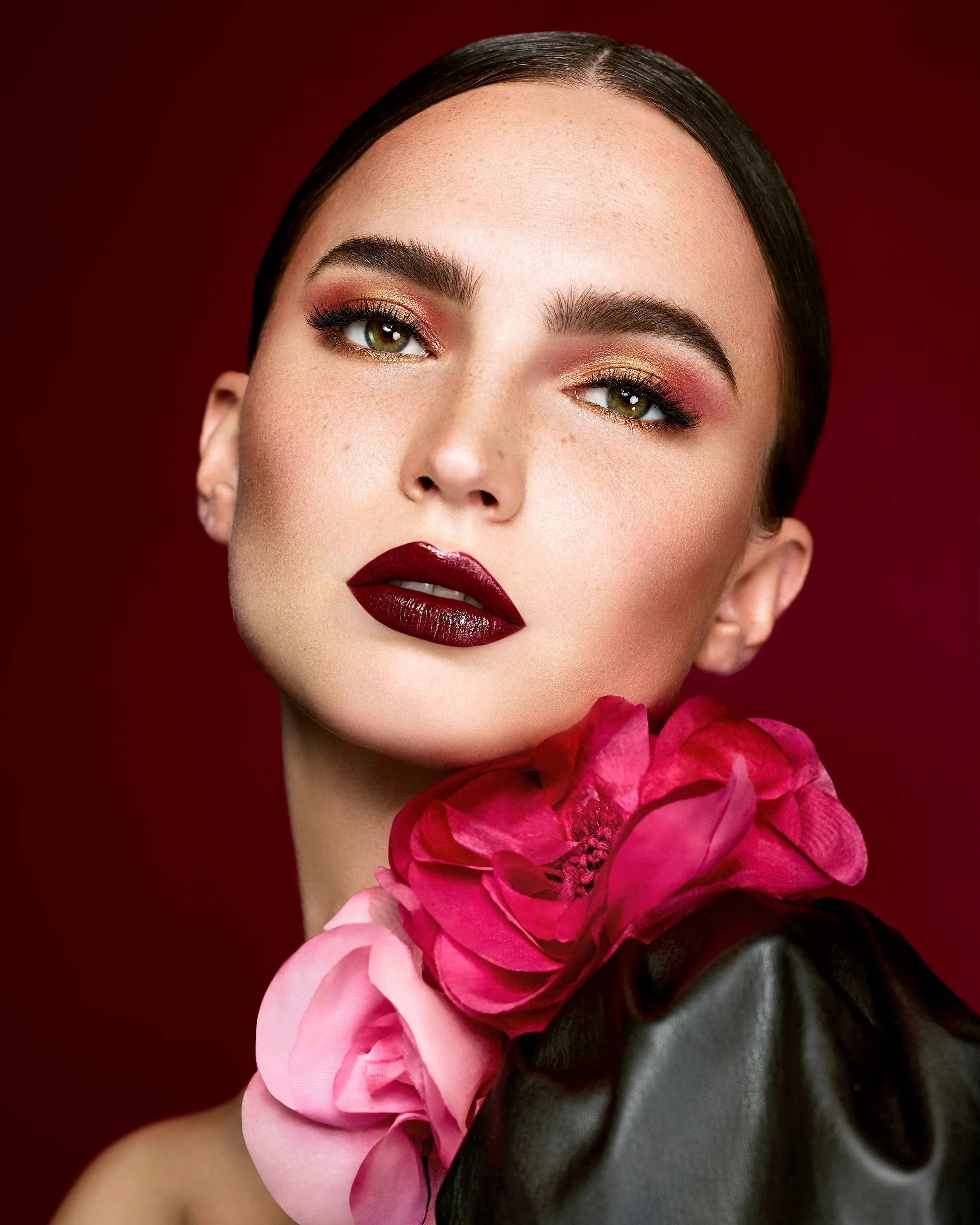 Frau mit dunkelrotem Lippenstift und rotem Lidschatten sowie roten Blüten am Hals, modernes nostalgisches Beauty-Kampagnenvisual für Makeup Factory, umgesetzt von imagespy.