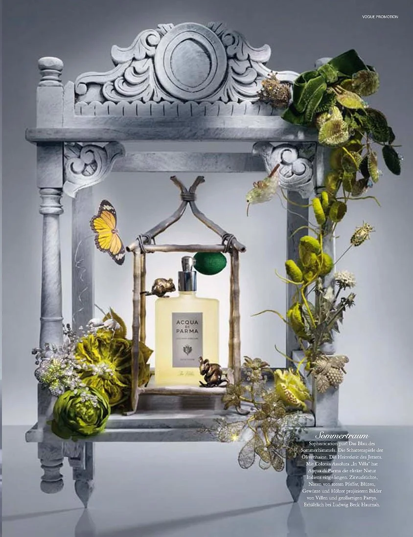 Stillleben-Fotografie von imagespy für VOGUE Hautnah: Ein Acqua di Parma  "In Villa" Flakon in einem barocken, geschnitzten grauen Rahmen, dekoriert mit grünen Satinblüten, einem Monarchfalter und goldenen Accessoires für Ludwig Beck.