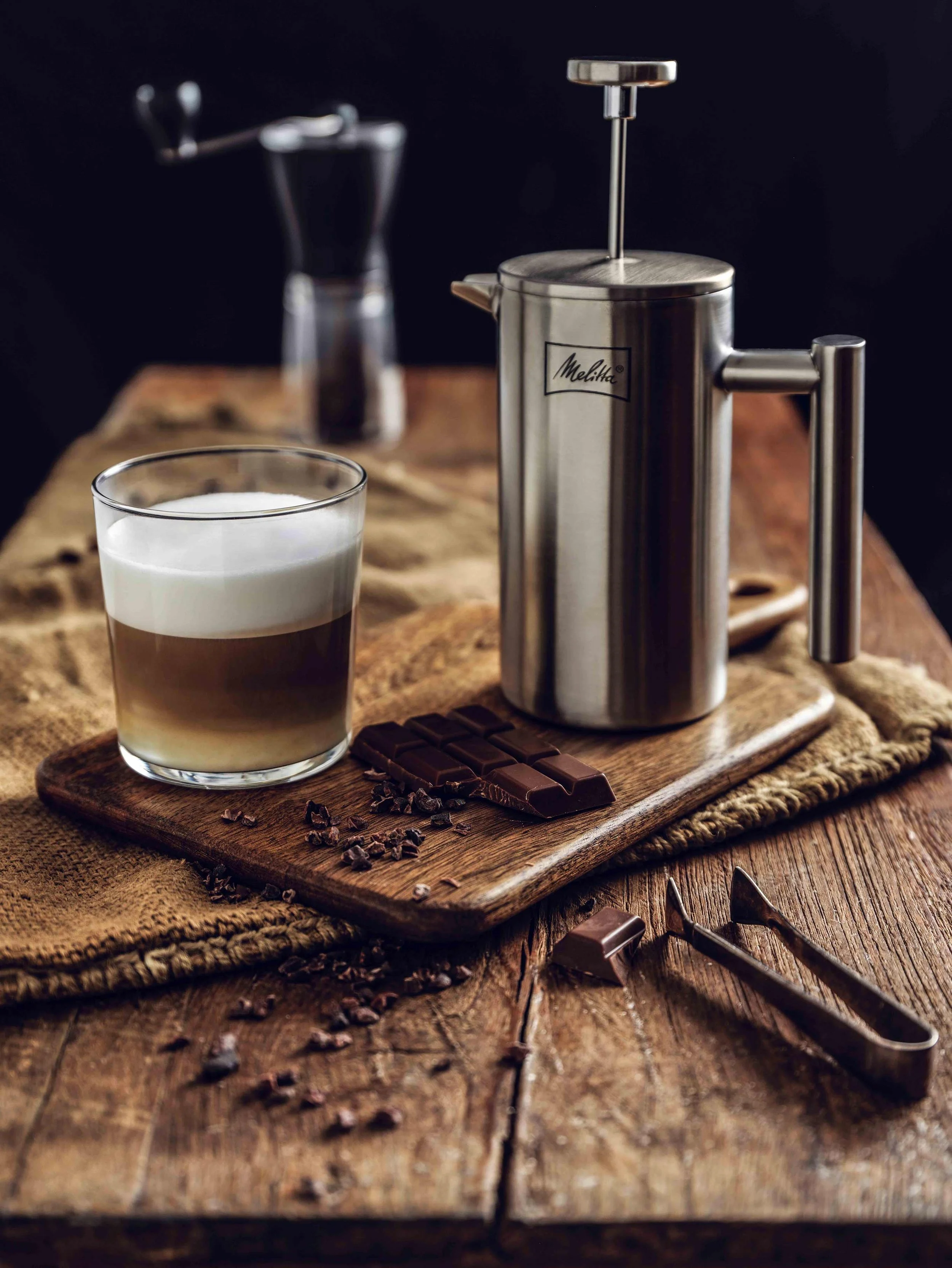 Professionelle Food-Fotografie von imagespy: Melitta French Press aus Edelstahl neben einem geschichteten Kaffee-Glas und dunkler Schokolade auf rustikalem Holz zum 111-jährigen Markenjubiläum.