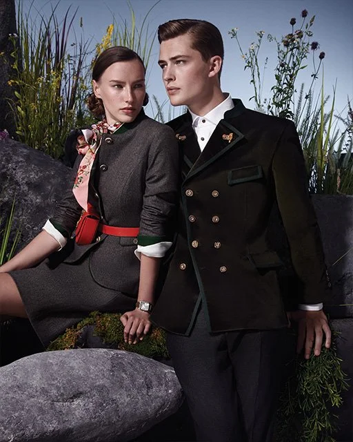 Couple in Tracht posiert auf großen Steinen vor einer hohen Wiese – moderne Trachteninszenierung von imagespy für Vogue und Lodenfrey.