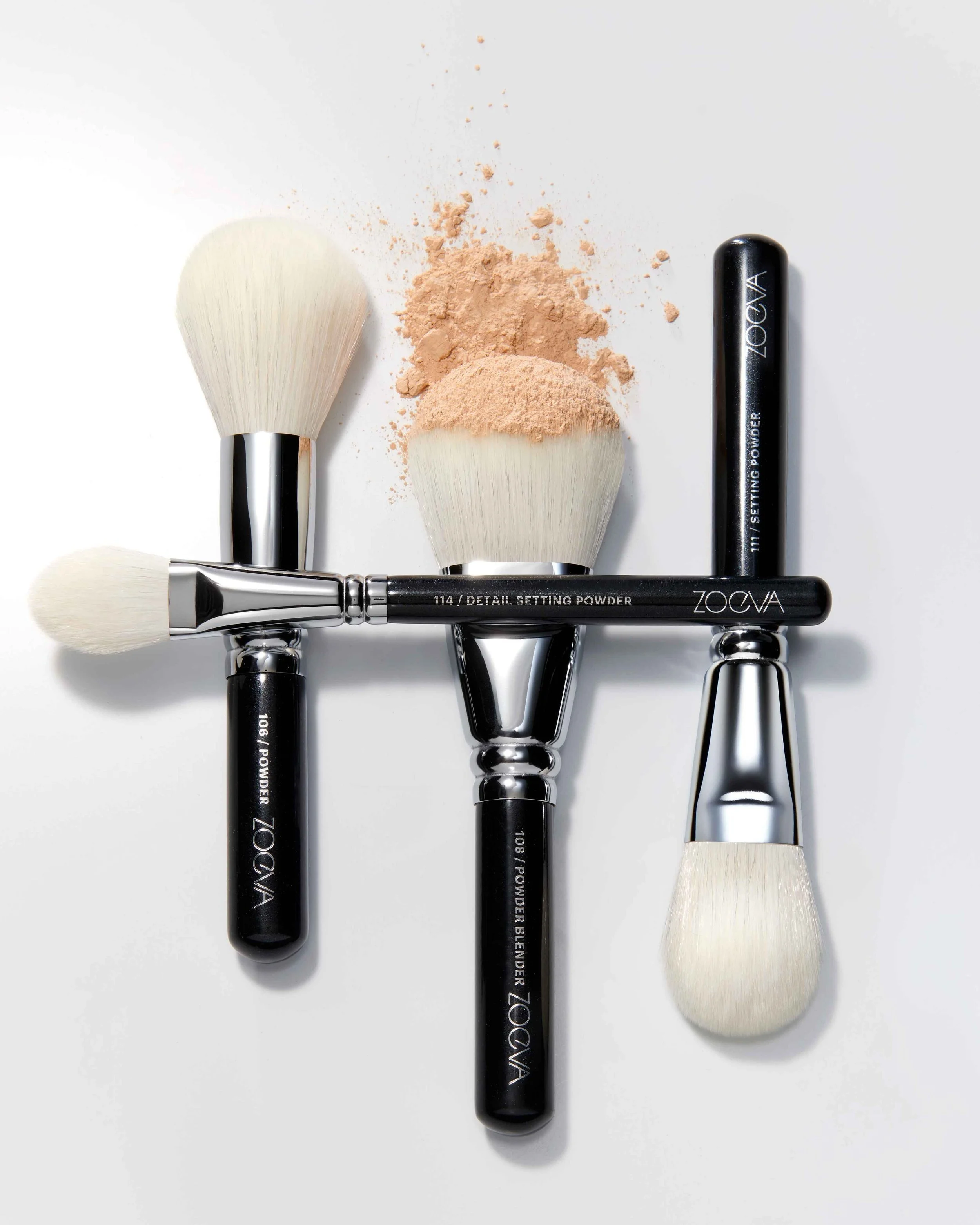 Zoeva Produktfotografie umgesetzt von imagespy, Anordnung von vier Make-up-Pinseln mit losem Puder auf weißem Untergrund, minimalistisches Branding und Design.