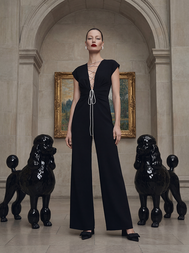 KI-generiertes Visual von imagespy im Rahmen einer KI-basierte Videoproduktion: Elegante Frau in einem schwarzen Jumpsuit mit Schnürung vor einem Gemälde in einer luxuriösen Kunstgalerie, flankiert von schwarzen Pudel-Skulpturen.