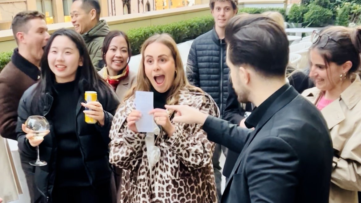 Group of people at a social gathering, smiling and engaging with each other outdoors, some holding drinks.
