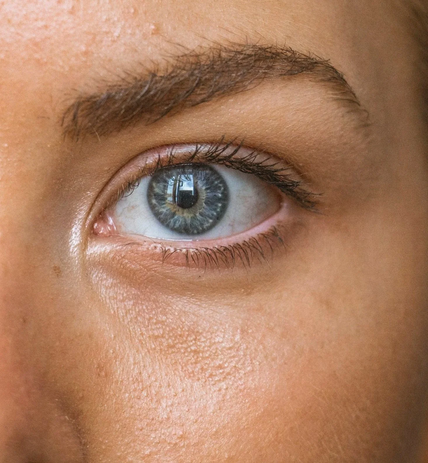 Close-up of a human eye with blue and gray iris, showing the reflection of a window.