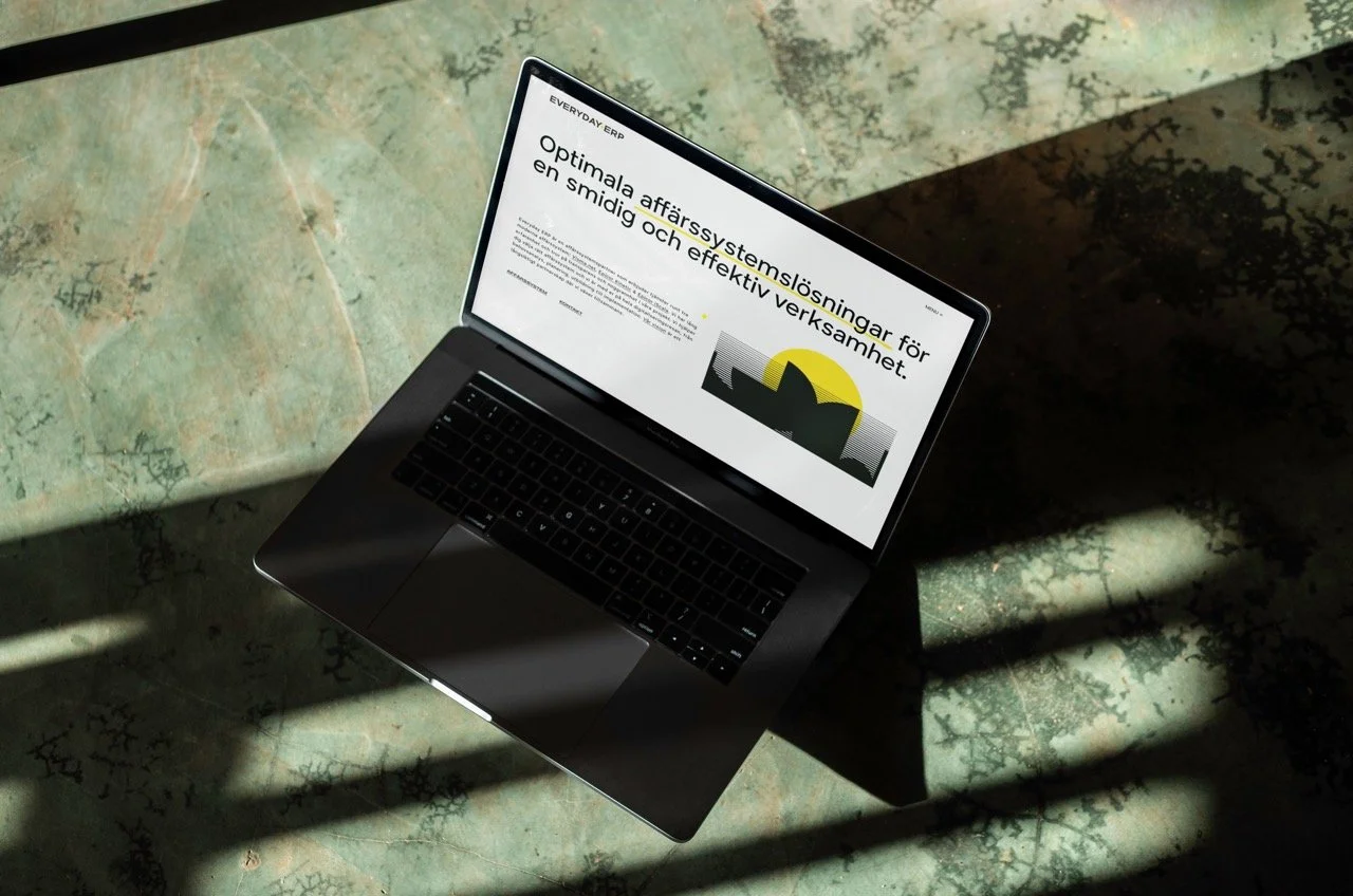 En bärbar dator som ligger på en gulaktig, sliten bordsyta med skuggor. Skärmen visar en presentation med rubrik om affärssystemlösningar.