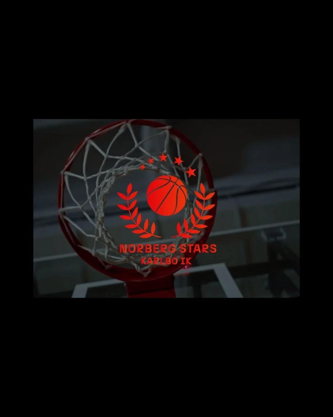 En basketkorg med en logo för Norberg Stars Karlbo IK, med en basketboll i mitten, omgiven av röda laurbär och stjärnor.