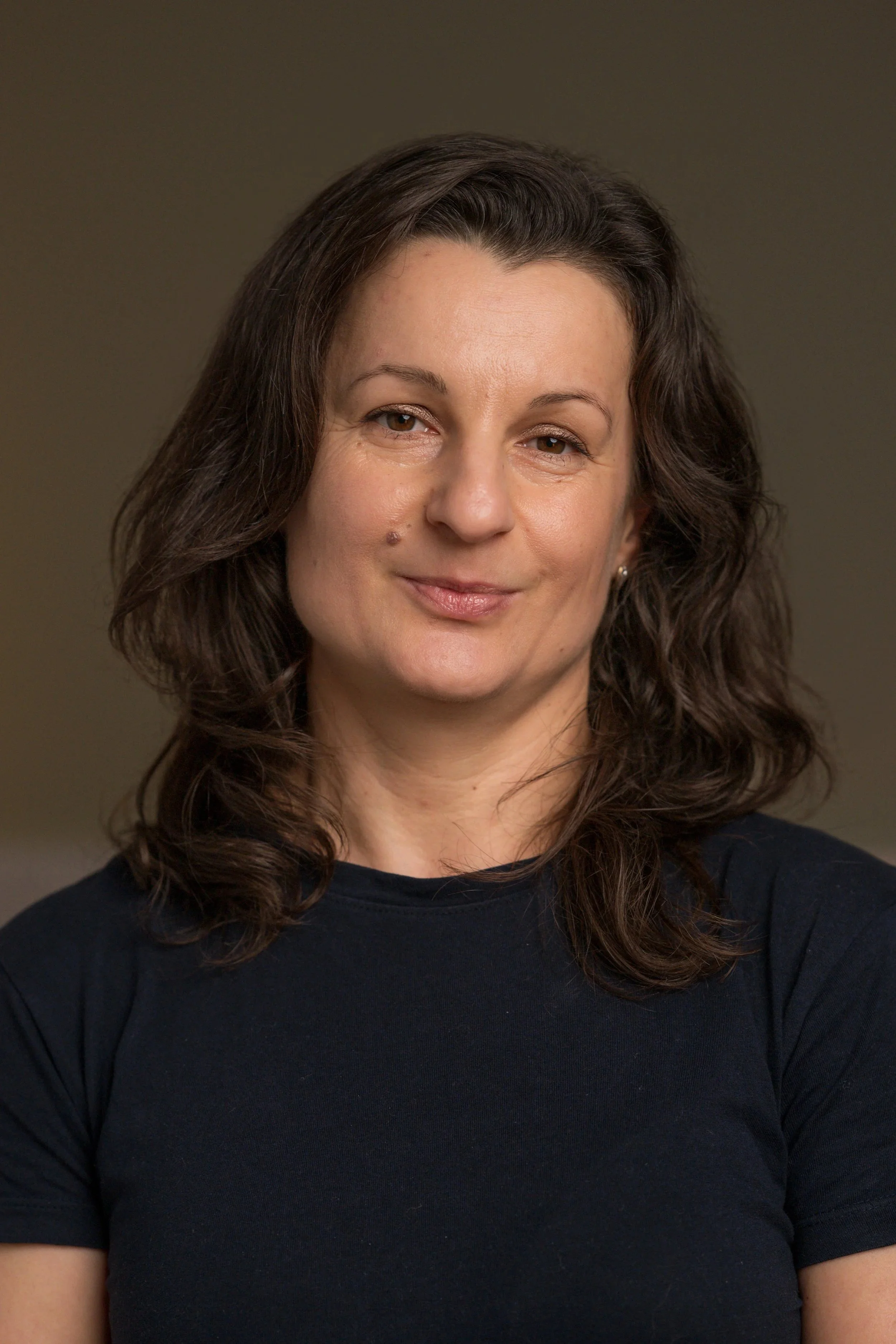 A woman smiling with long brown hair against a plain background.