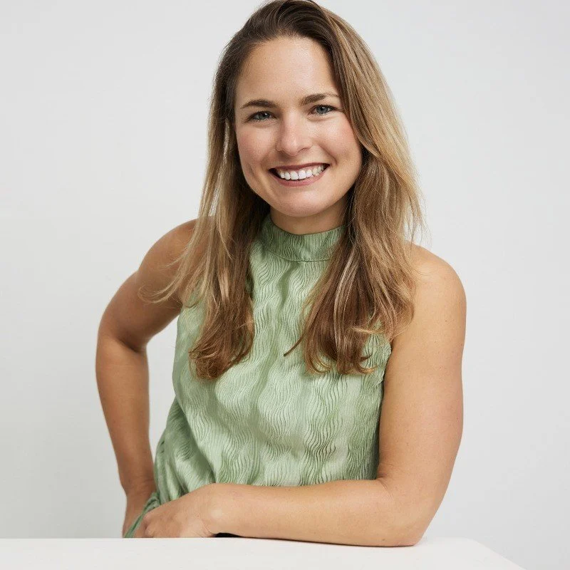 A young woman with long light brown hair, wearing a light green sleeveless top, smiling and posing against a plain white background.