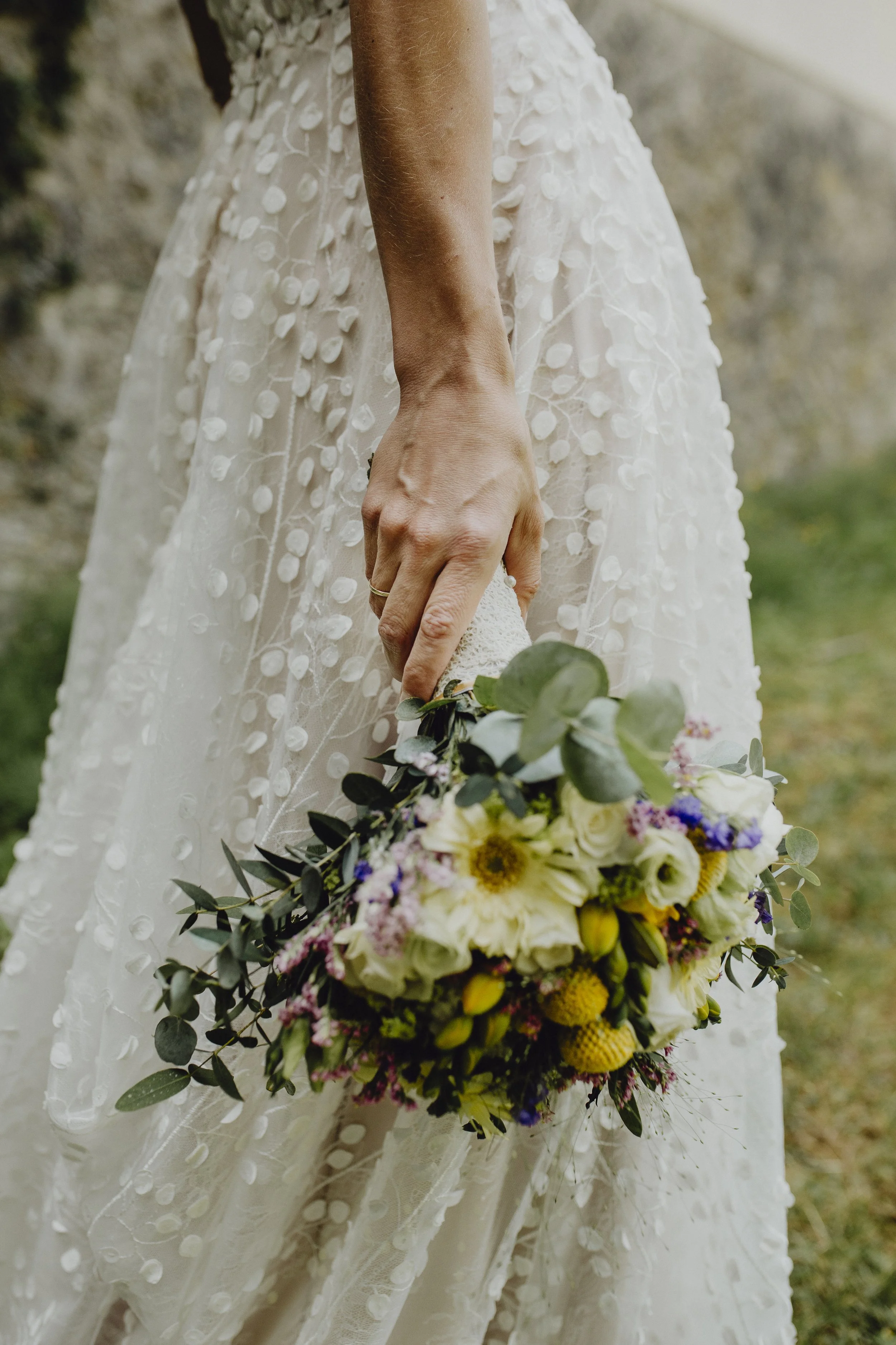 Nahaufnahme einer Braut, die ein Blumenbouquet locker in ihrer Hand hält.