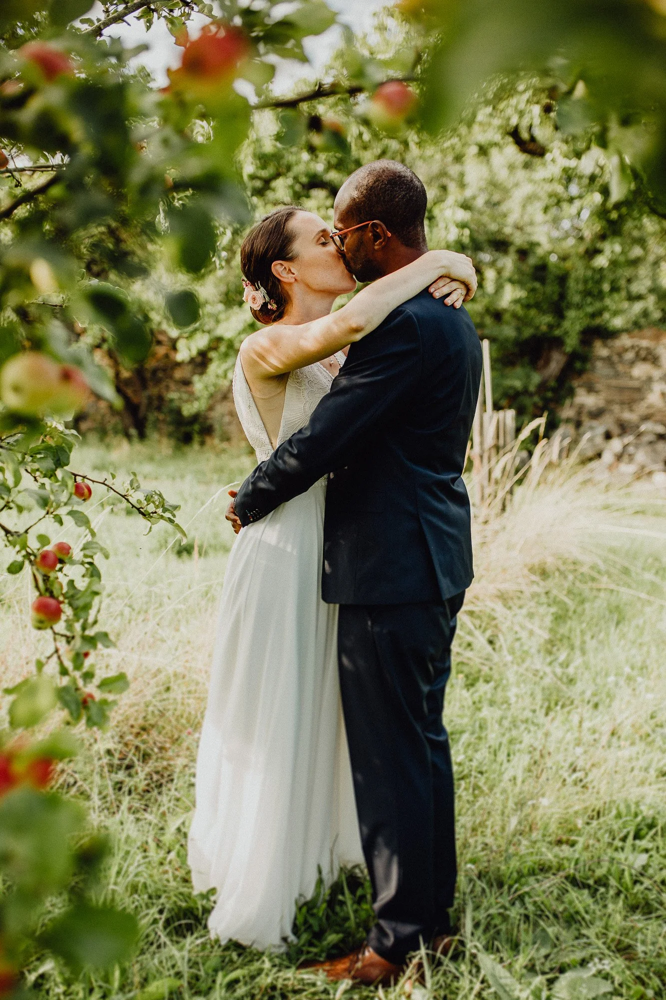 Ein Brautpaar küss sich im Grünen bei einem Hochzeitsshooting in einem Garten mit unscharfem Grün im Vordergrund.
