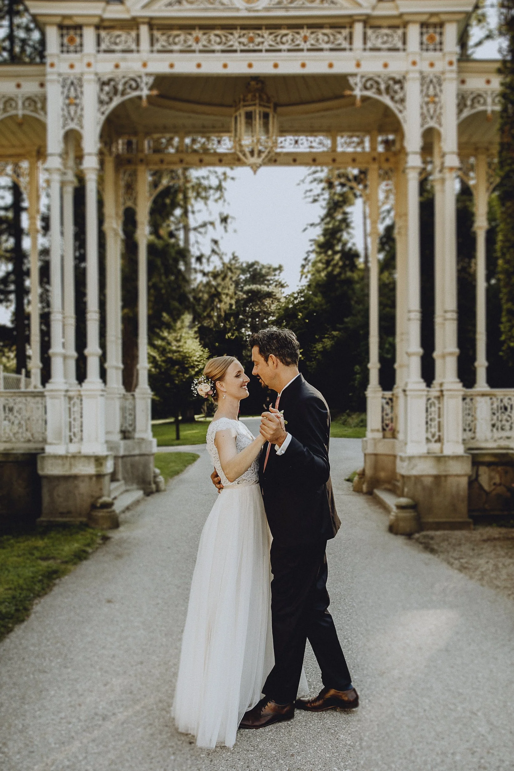 Ein Brautpaar tanzt unter einer kunstvollen, weißen Pavillon im Freien bei Sonnenuntergang.
