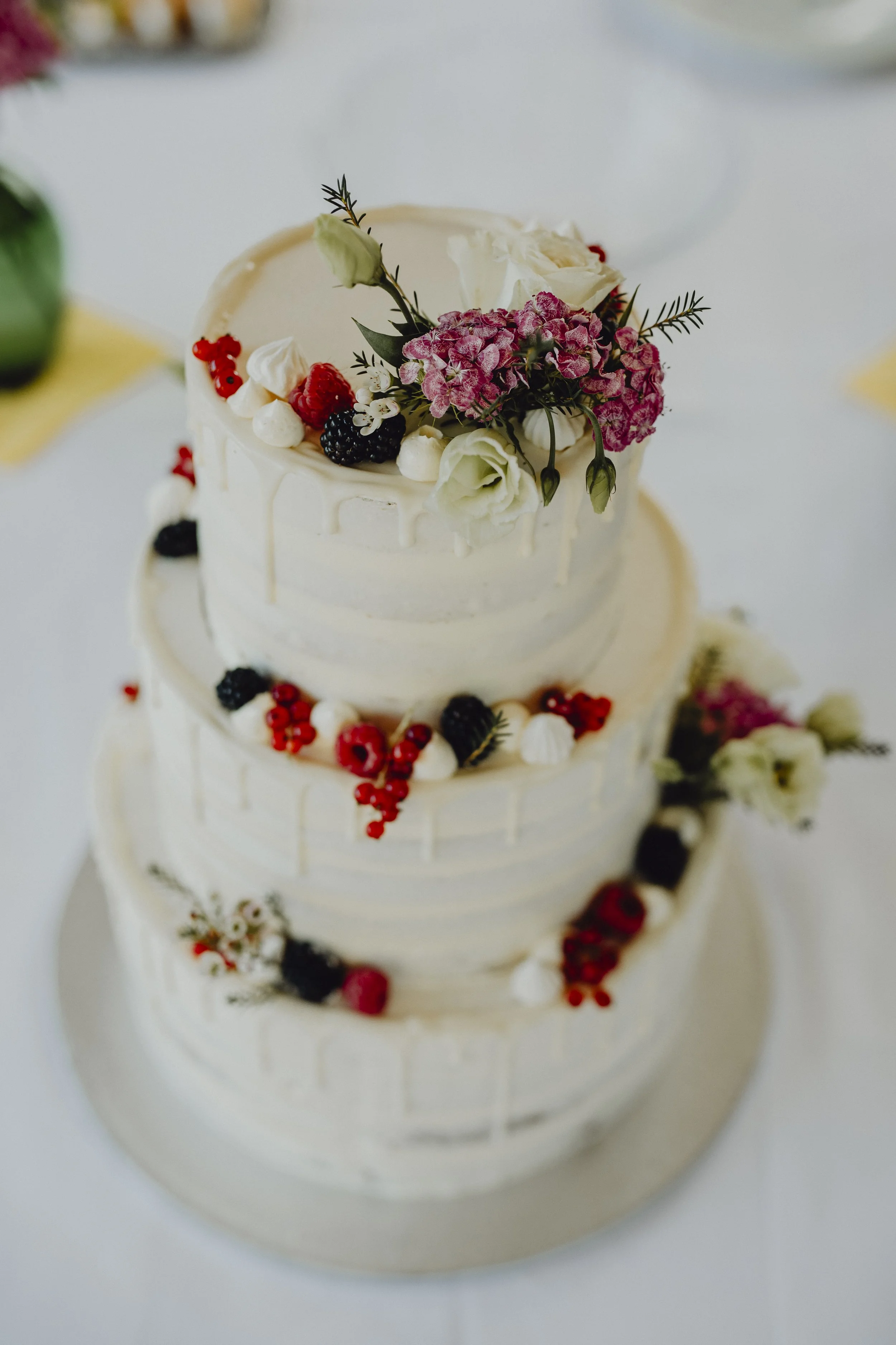 Dreistöckige Hochzeitstorte mit weißer Glasur, verziert mit frischen Blumen und Beeren.