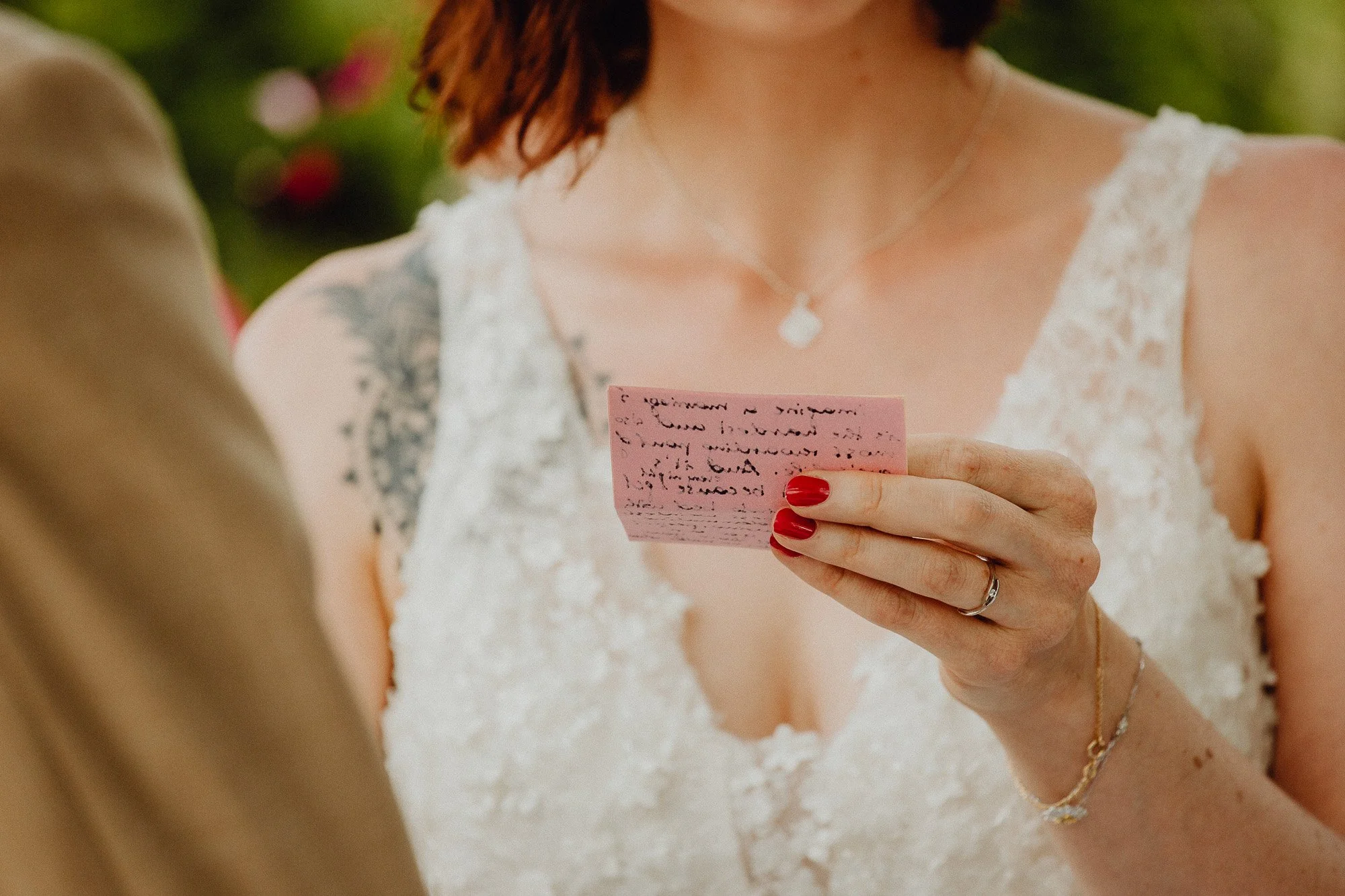 Eine Frau in Weiß liest eine handgeschriebene Notiz auf einem pinken Zettel während einer Hochzeit.