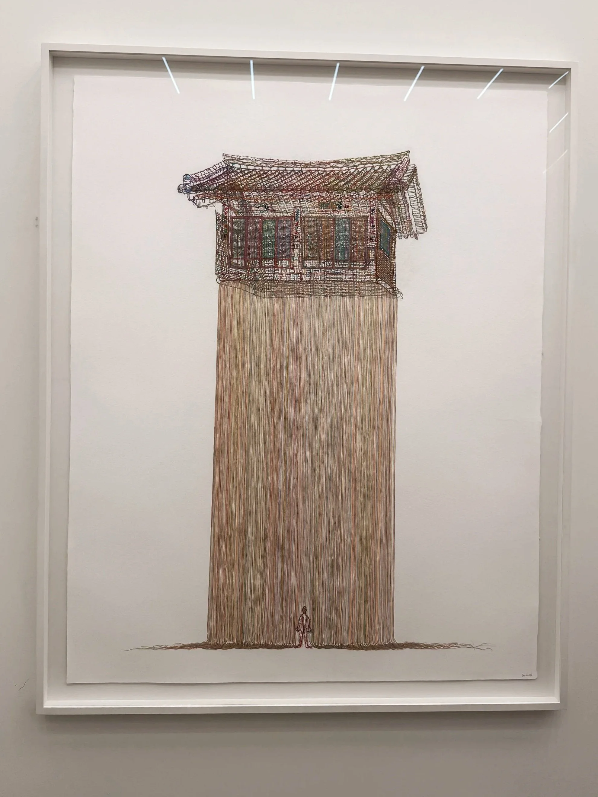 A thread drawing by Do Ho Suh showing a traditional Korean house suspended above long strands of thread, with a small human figure standing below.