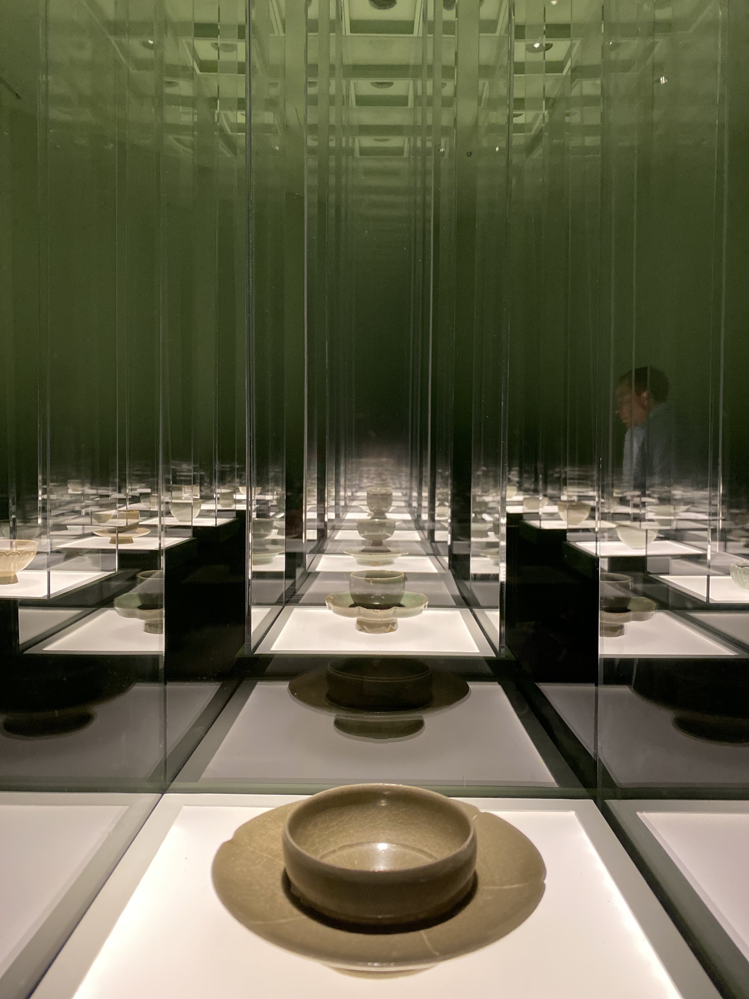 Display of ceramic bowls and plates reflected repeatedly in mirrors, creating an infinity effect, in a museum or gallery setting.