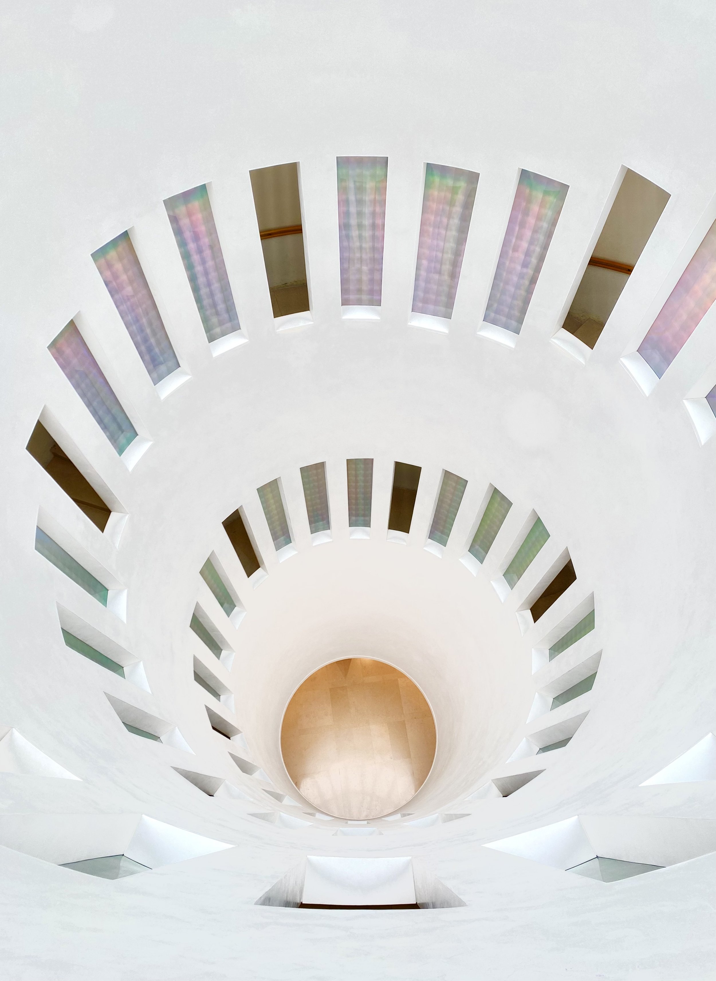 Abstract architectural interior with circular design and radial slits allowing colorful light entry.