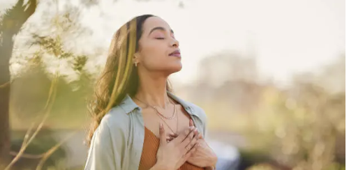 Woman with eyes closed, embracing nature outdoors in sunlight.