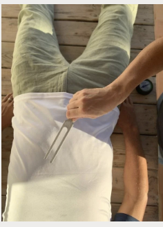 A person lying on a wooden surface, with another person's hand holding a metal tool near their abdomen.