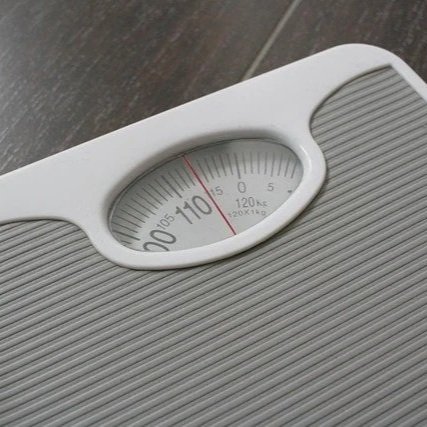 A close-up of a bathroom scale with a dial showing approximately 0 pounds.