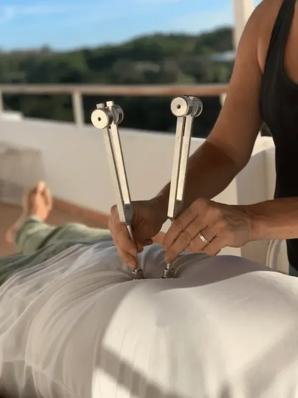Person receiving chiropractic adjustment with specialized tools on lower back, with another person lying down on a table.