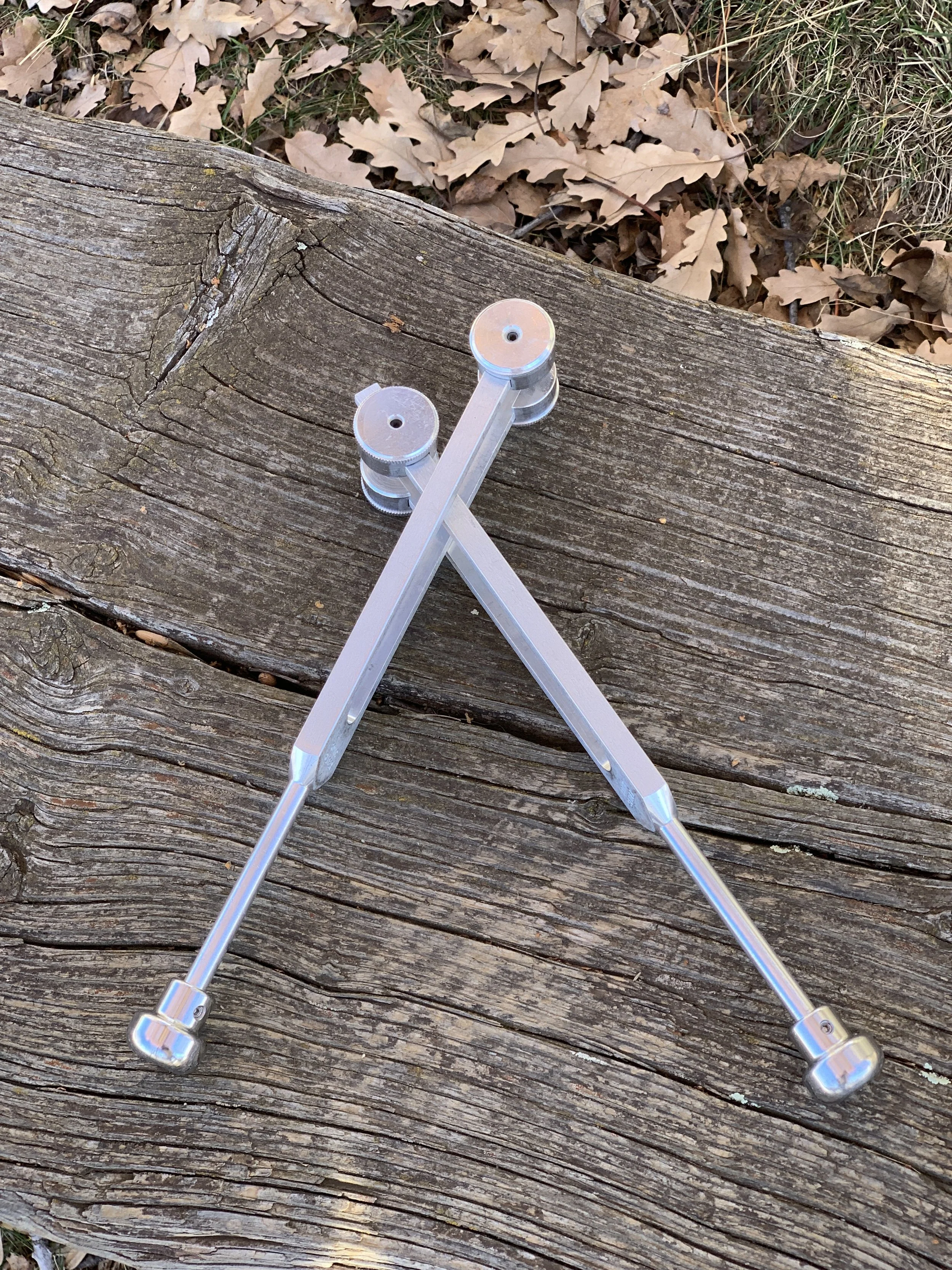 Two calipers placed on a weathered wooden surface with fallen brown leaves and grass in the background.