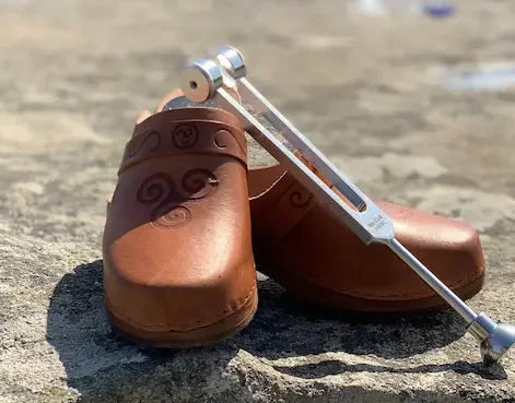 A pair of brown leather shoes with a metal device attached to them, placed on a rough outdoor surface.