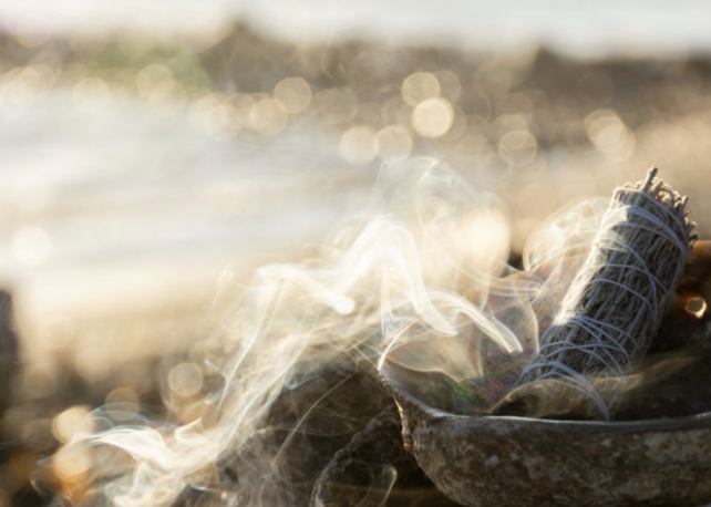 Smoldering sage bundles burning in a bowl with smoke rising, outdoors during daytime.