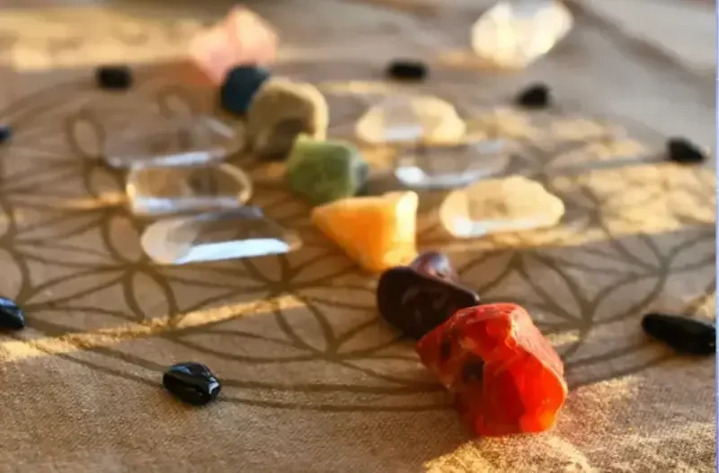 A crystal grid with various gemstones arranged on a fabric surface, centered within a geometric pattern.
