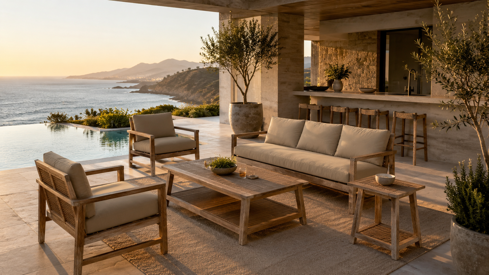 Open outdoor living space overlooking a coastal view, with beige cushioned wooden furniture, potted trees, and a pool, illuminated by sunset light.
