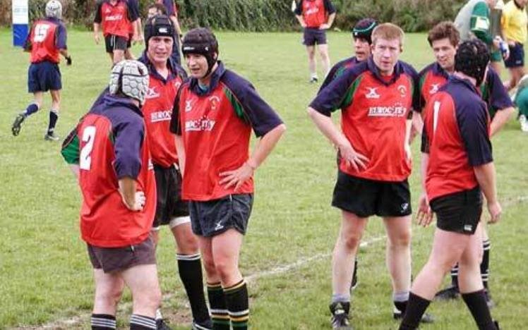 Rugby players in red and blue jerseys on a field, wearing helmets, standing in a group.