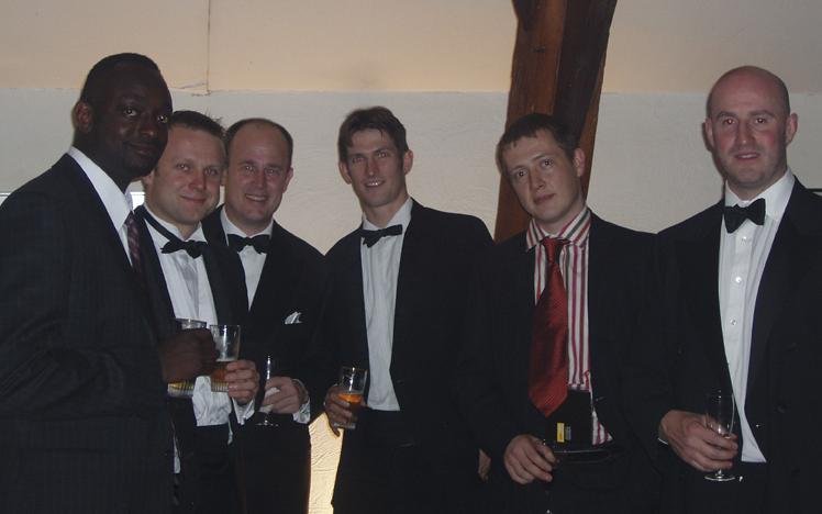 Group of men in tuxedos holding drinks at a formal event.