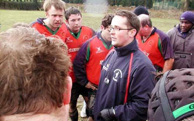 Rugby players and coach huddled on field during game