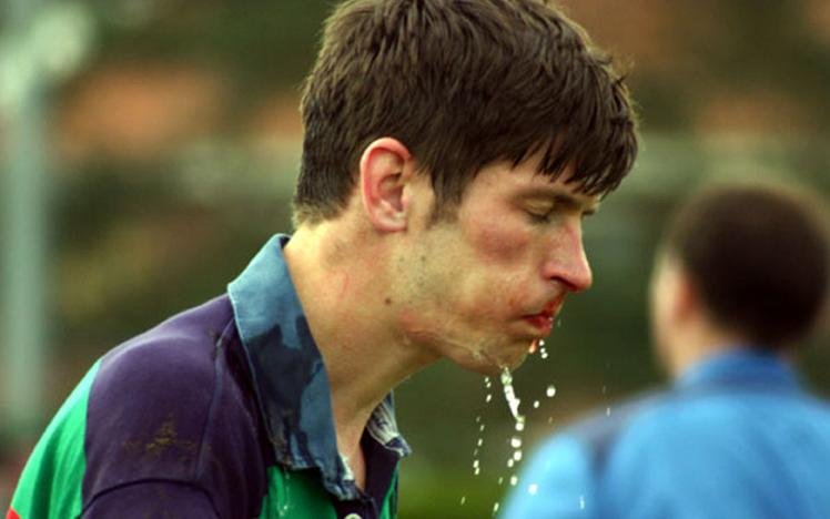 Person spitting water during a sports game, wearing a multicolored sports jersey, with blurred background.