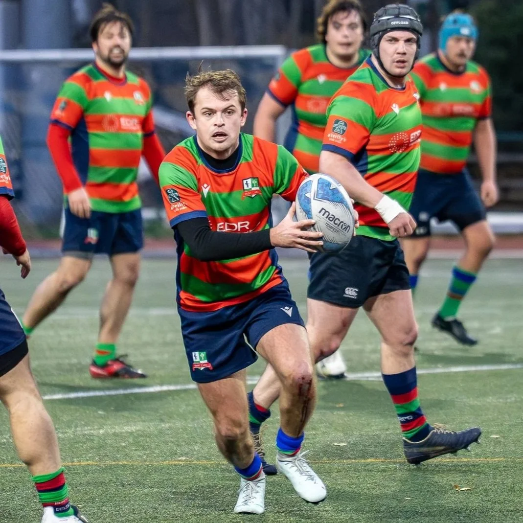 Rugbyspelers in actie tijdens een wedstrijd, in blauwe en rode uniformen, strijdend om de bal op een grasveld.