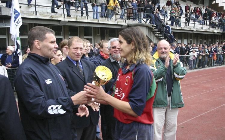 Sports award ceremony featuring athletes and officials on a track, with one player receiving a trophy and a crowd in the background.
